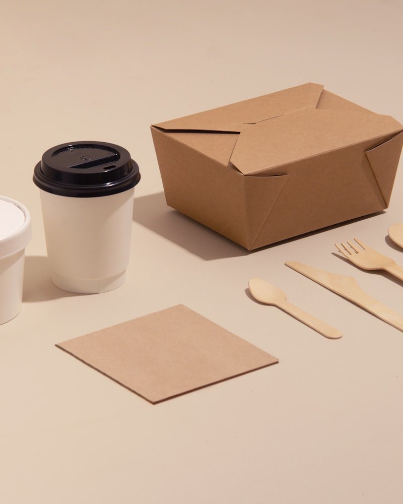 Flat lay of a paper hot cup, kraft takeout container, wooden cutlery and a napkin