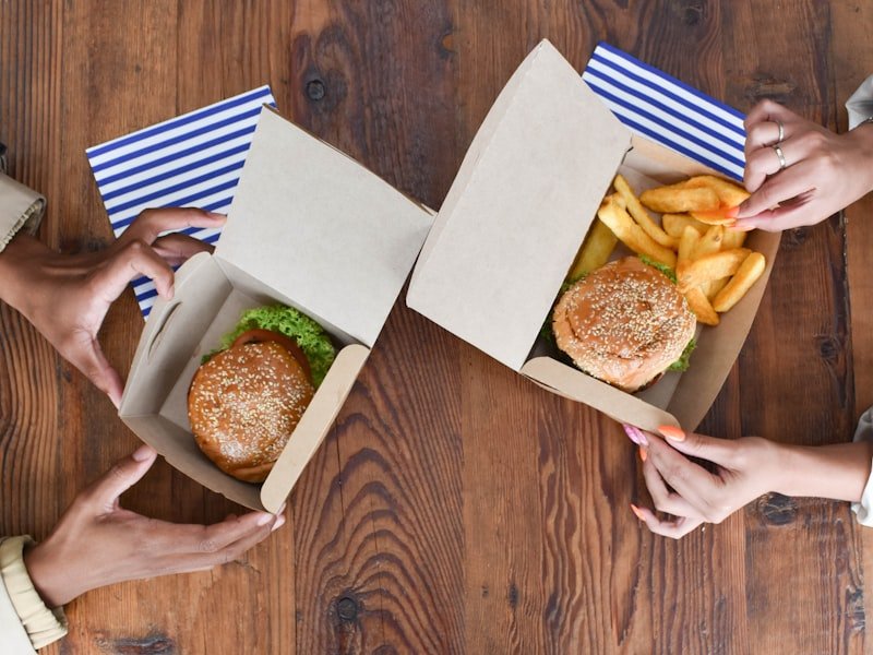 Two people opening kraft takeout containers of food on a wooden table